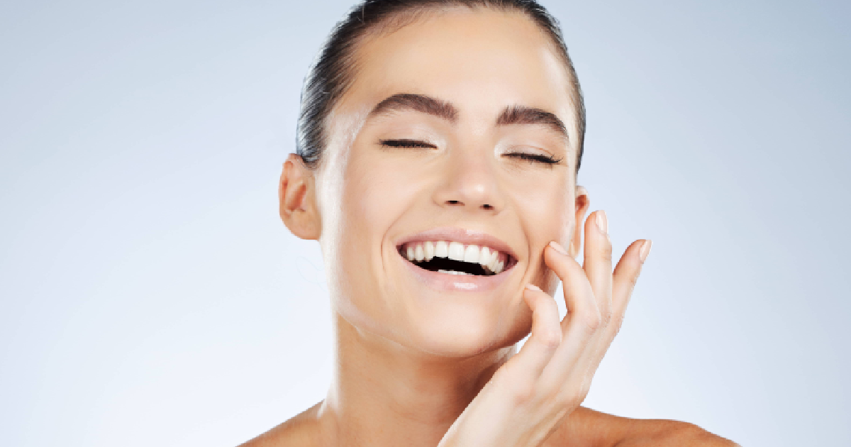 Smiling woman with glowing skin and closed eyes, gently touching her face after Medical Grade Skincare treatment in Destin, FL.