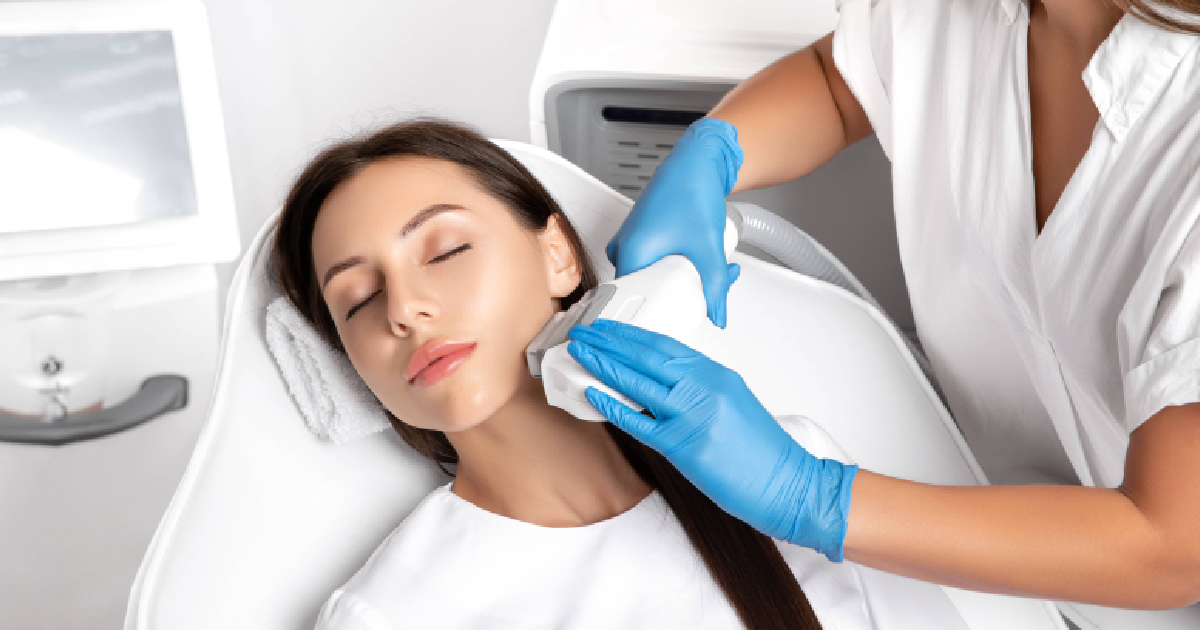 Young woman receiving an IPL photofacials in Destin, FL, lying relaxed with eyes closed while a professional in blue gloves treats her face with a handheld device