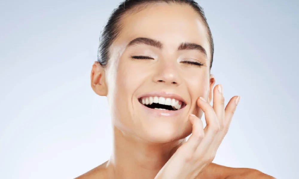 Smiling woman with glowing skin and closed eyes, gently touching her face after Medical Grade Skincare treatment in Destin, FL.